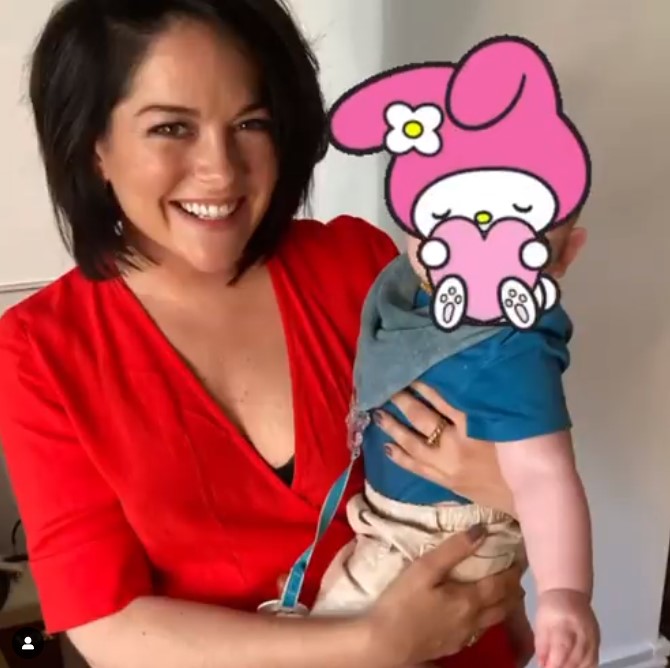 Sarah Greene holding her son while using a sticker to hide his face