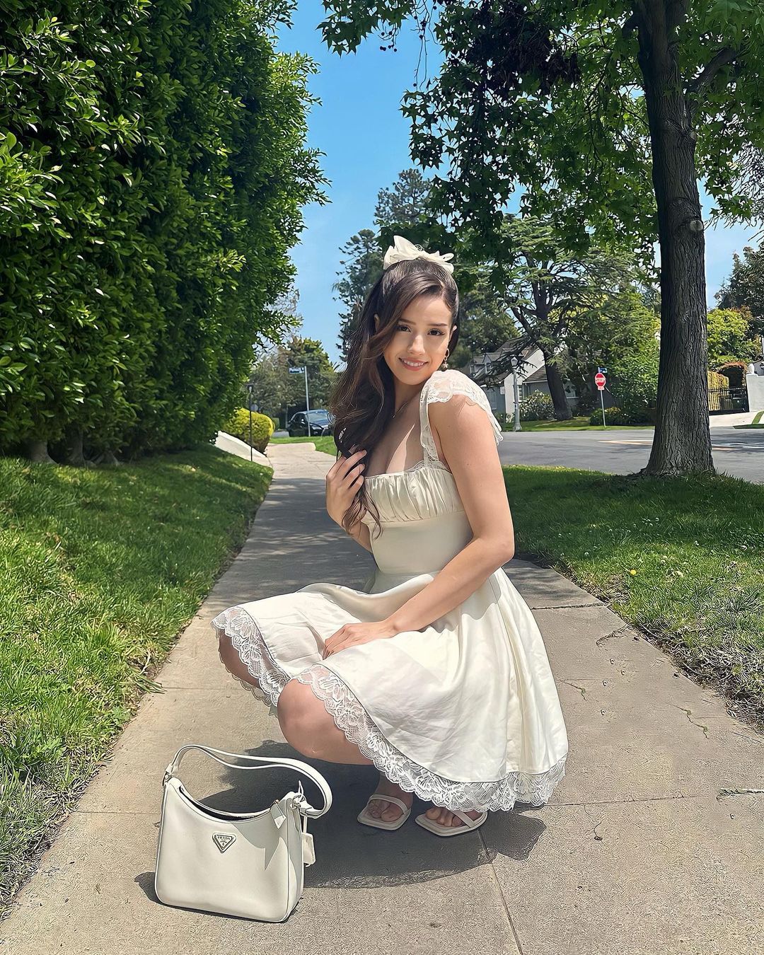 Pokimane wearing a white outfit and taking pictures in a sidewalk
