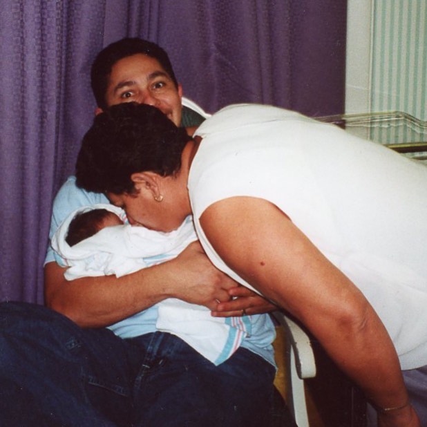 A baby Enya Umanzor being held by her father while being kissed by her grandmother